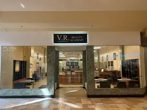 Storefront entrance for V.R. Beauty Professional Academy in an indoor shopping center, with the academy sign above glass doors and salon workstations visible inside.