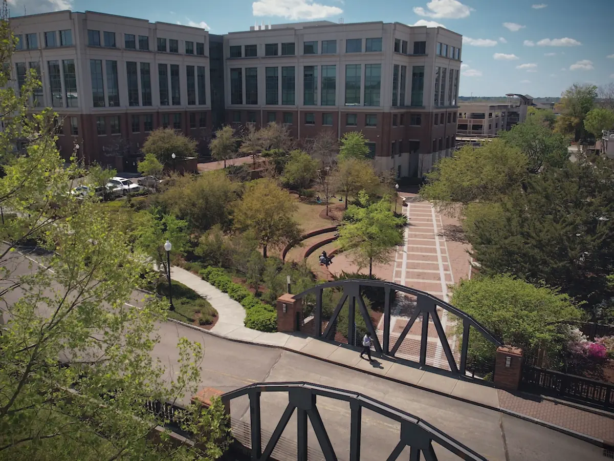 Aerial view of Cape Fear Community College buildings, landscaped walkways, trees, and a pedestrian bridge.