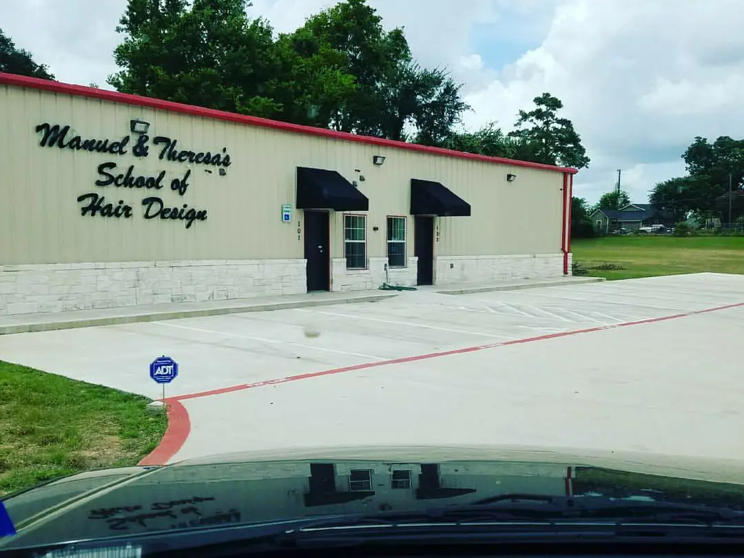 Exterior of Manuel & Theresa’s School of Hair Design, a cream-colored building with red trim, black awnings, two entrance doors, and the school name painted on the front wall.