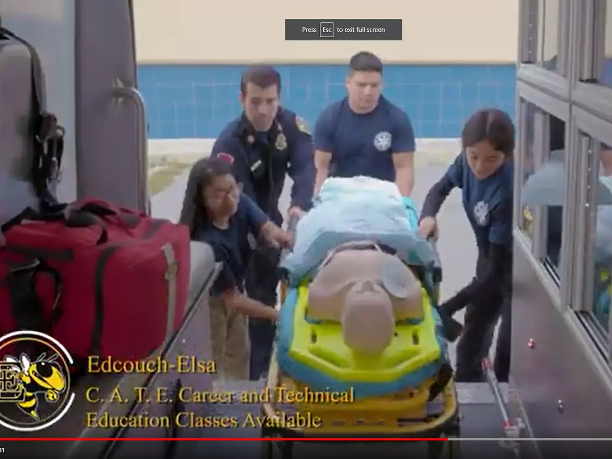 Students and instructors in a school hallway move a training mannequin on a wheeled stretcher during an emergency medical services exercise; Edcouch-Elsa CATE branding appears at the lower left.