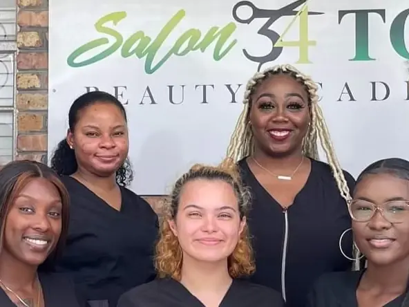 Group of students standing and seated in front of a Salon 34 Too Beauty Academy backdrop.