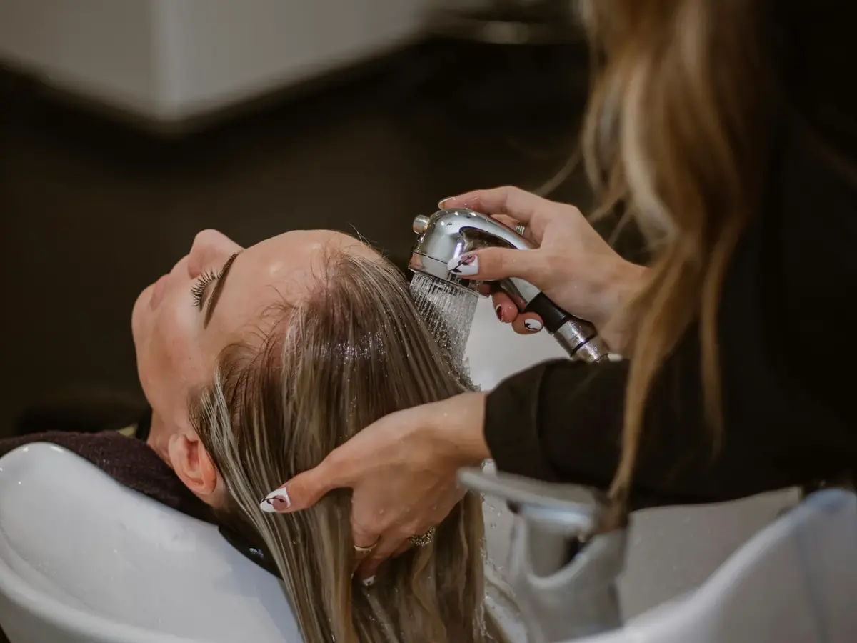 A cosmetology student washes a client’s hair at a salon shampoo station.