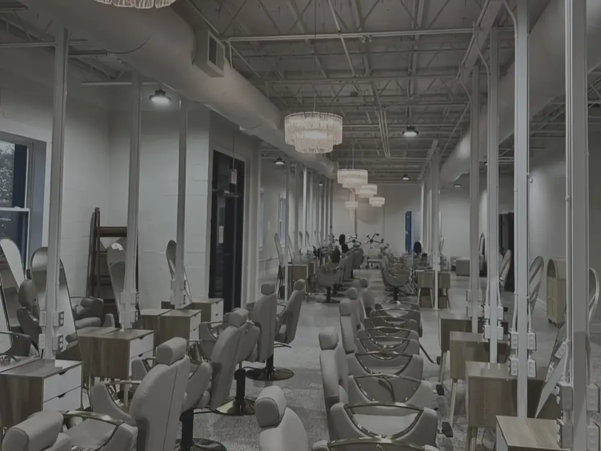 Interior of a cosmetology academy salon with rows of styling stations, salon chairs, and shampoo basins extending down the room.