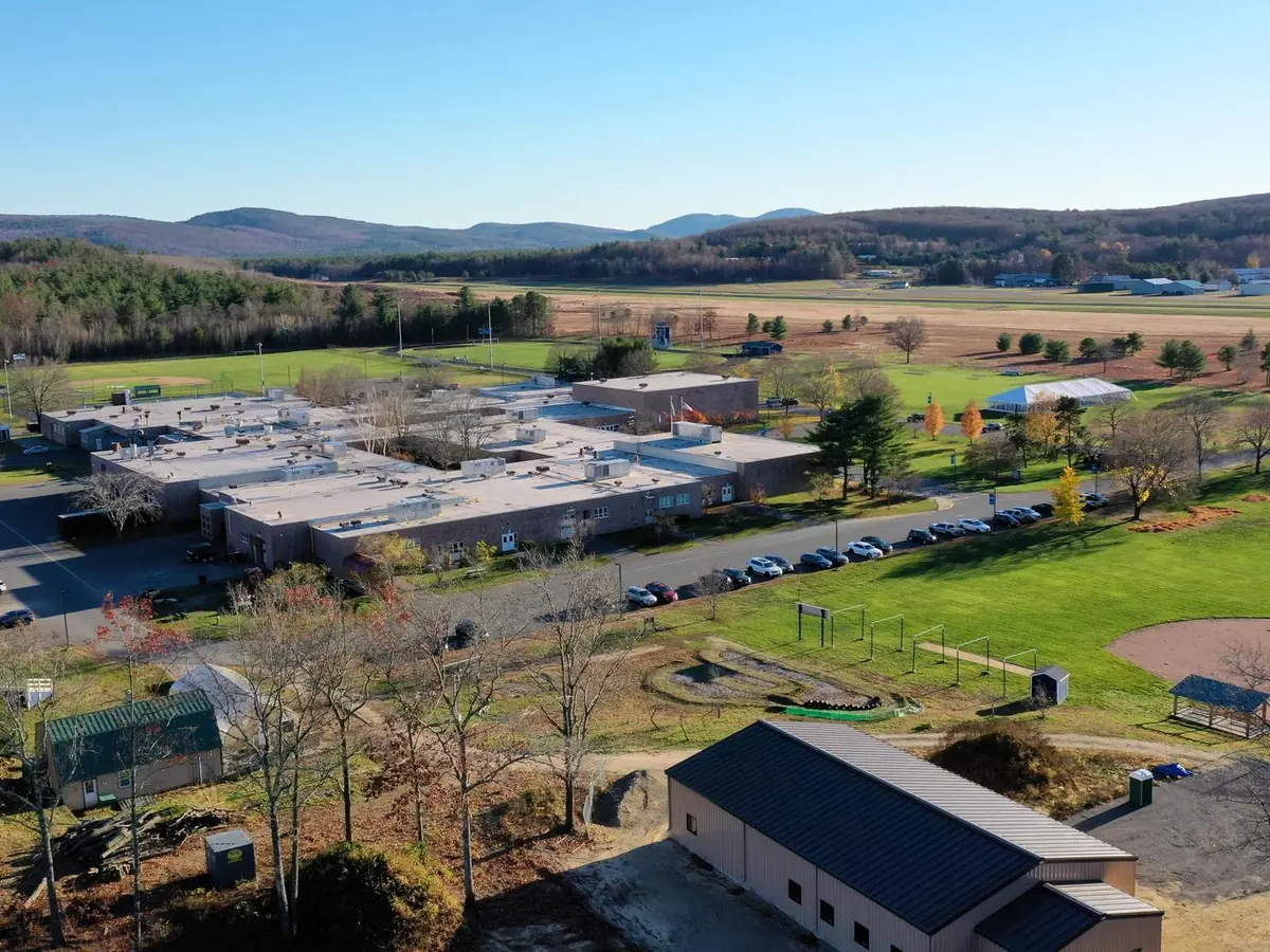 Aerial view of Franklin County Technical School campus buildings, parking areas, lawns, sports fields, and surrounding hills under a clear blue sky.