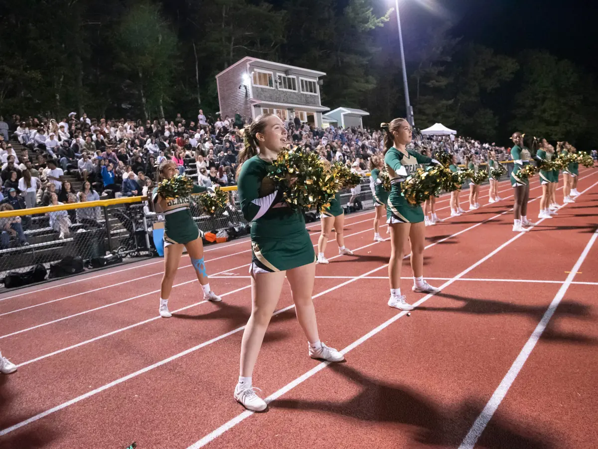Cheerleaders performing on a running track at night in front of a crowded grandstand.