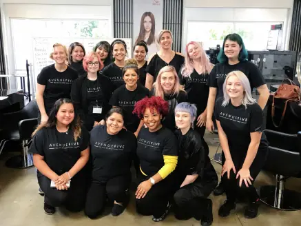 Group of Avenue Five Institute students posing together inside a salon classroom, with styling stations and mirrors behind them.