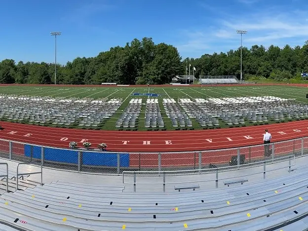 Panoramic view of Nashoba Valley Technical High School's outdoor track and football stadium, with bleachers in the foreground and wooded grounds beyond.