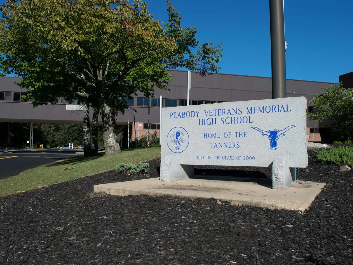 Exterior of Peabody Veterans Memorial High School with a large campus monument sign in front, trees, landscaping, and the school building behind it.