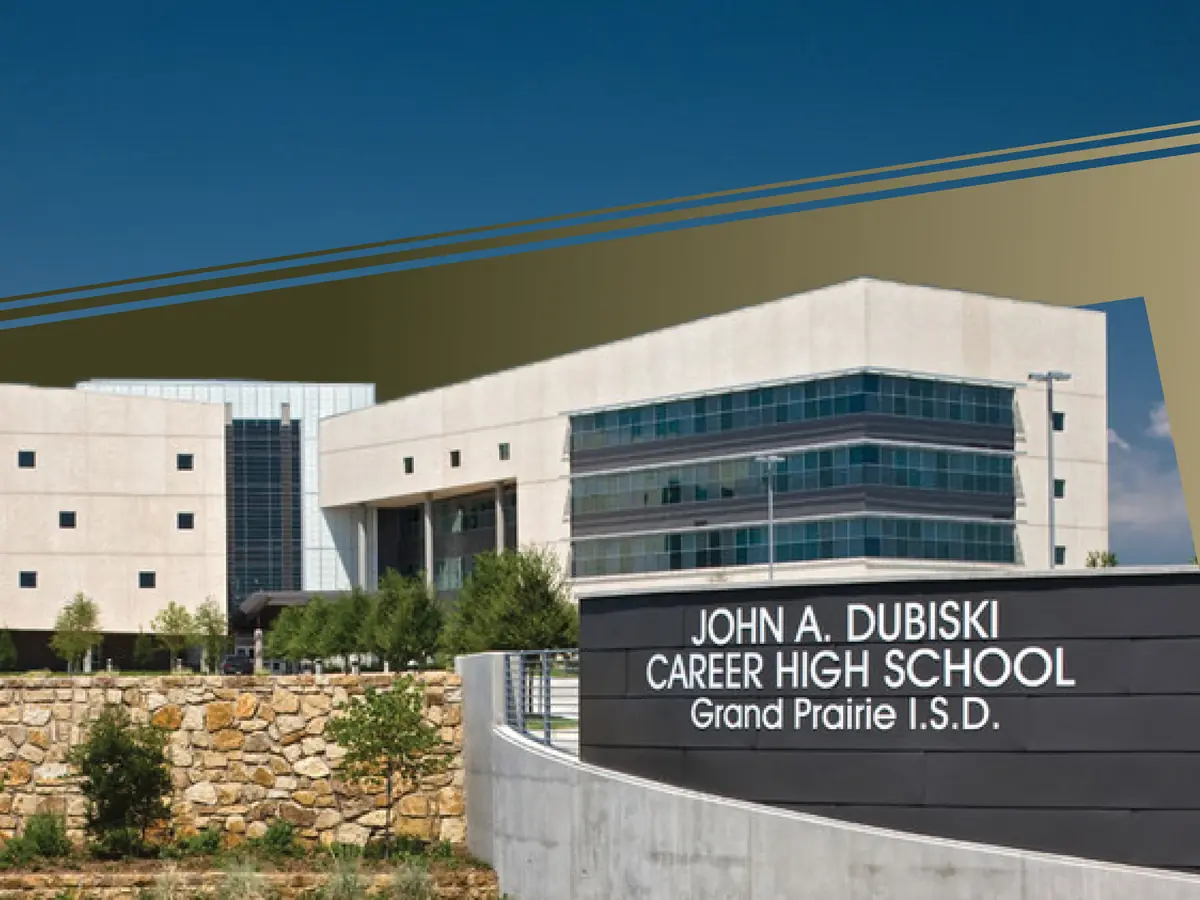 A large modern white school building behind a black monument sign that reads "JOHN A. DUBISKI CAREER HIGH SCHOOL" and "Grand Prairie I.S.D." under a blue sky.