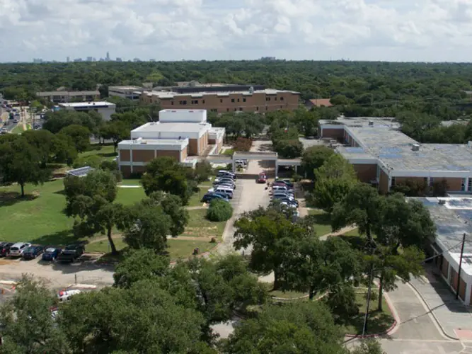 Aerial view of Crockett Early College High School campus with multiple school buildings, parking lots, trees, and surrounding Austin neighborhood.