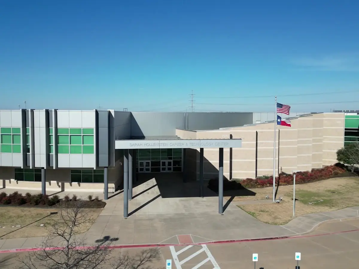 Exterior entrance of the Hollenstein Career and Technology Center, showing the modern gray-and-green building facade, covered walkway, flagpoles, and front drive.