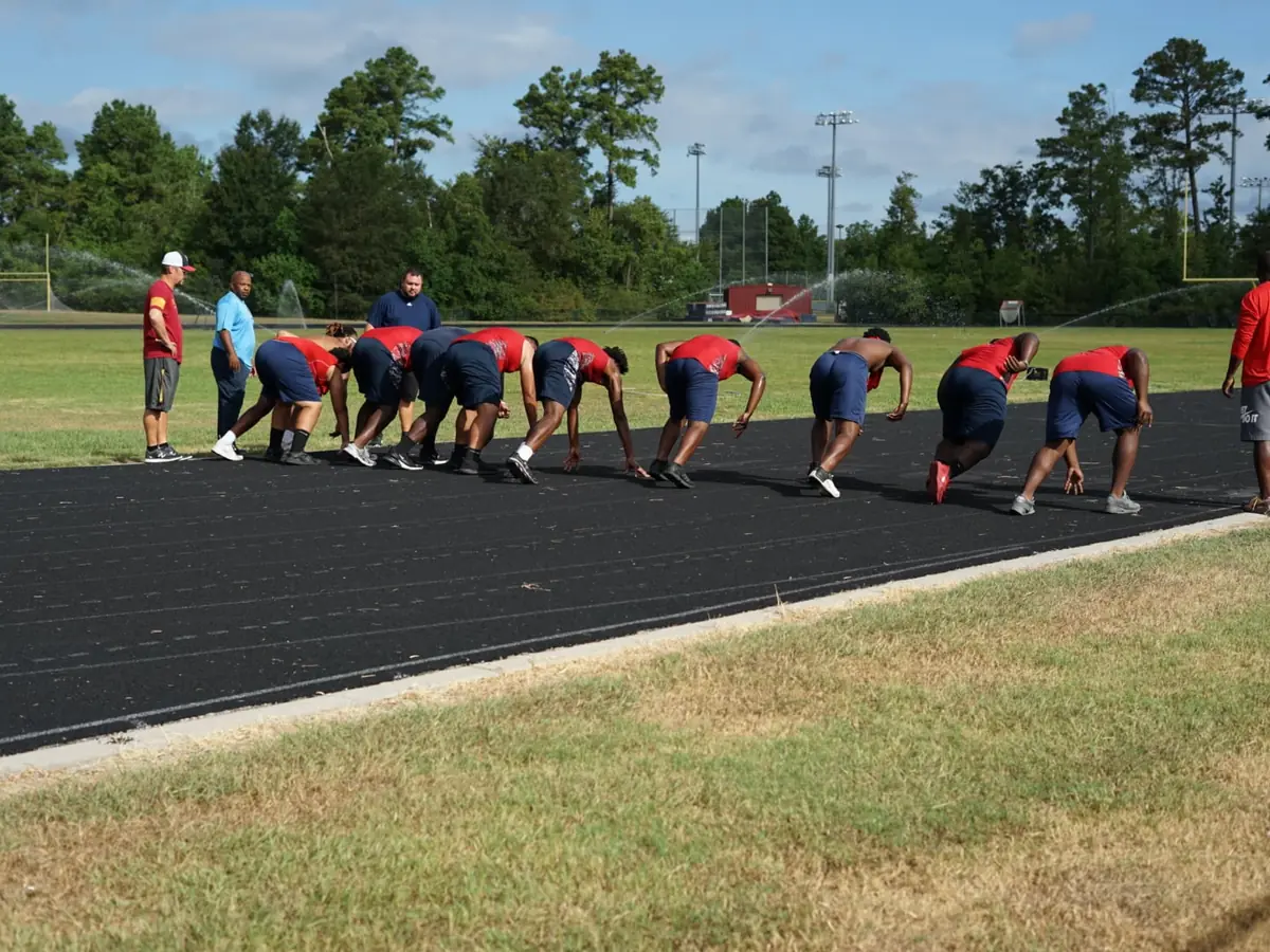 Davis High School track athletes crouch at the starting line on an outdoor track beside a grassy athletic field and trees.