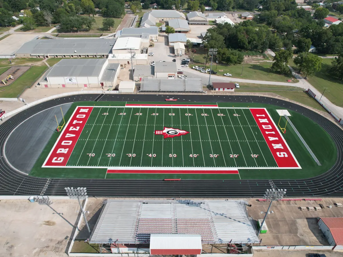 Aerial view of Groveton High School’s football stadium and surrounding school buildings, with “GROVETON” and “INDIANS” painted in the end zones.