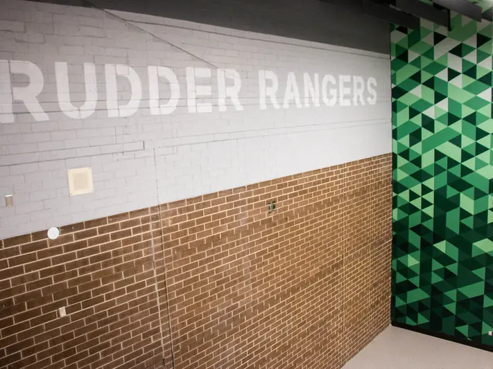 Interior hallway at Rudder High School with white “RUDDER RANGERS” lettering on a gray-and-brick wall beside a green geometric-patterned doorway.