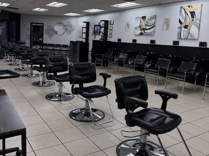 Bright cosmetology training salon with rows of black styling chairs, mirrors, fluorescent ceiling lights, and wall artwork.