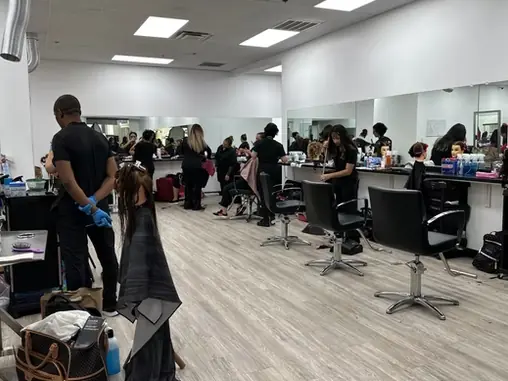 Bright beauty academy salon with mirrored walls, styling stations, salon chairs, students and instructors working on hair throughout the room.