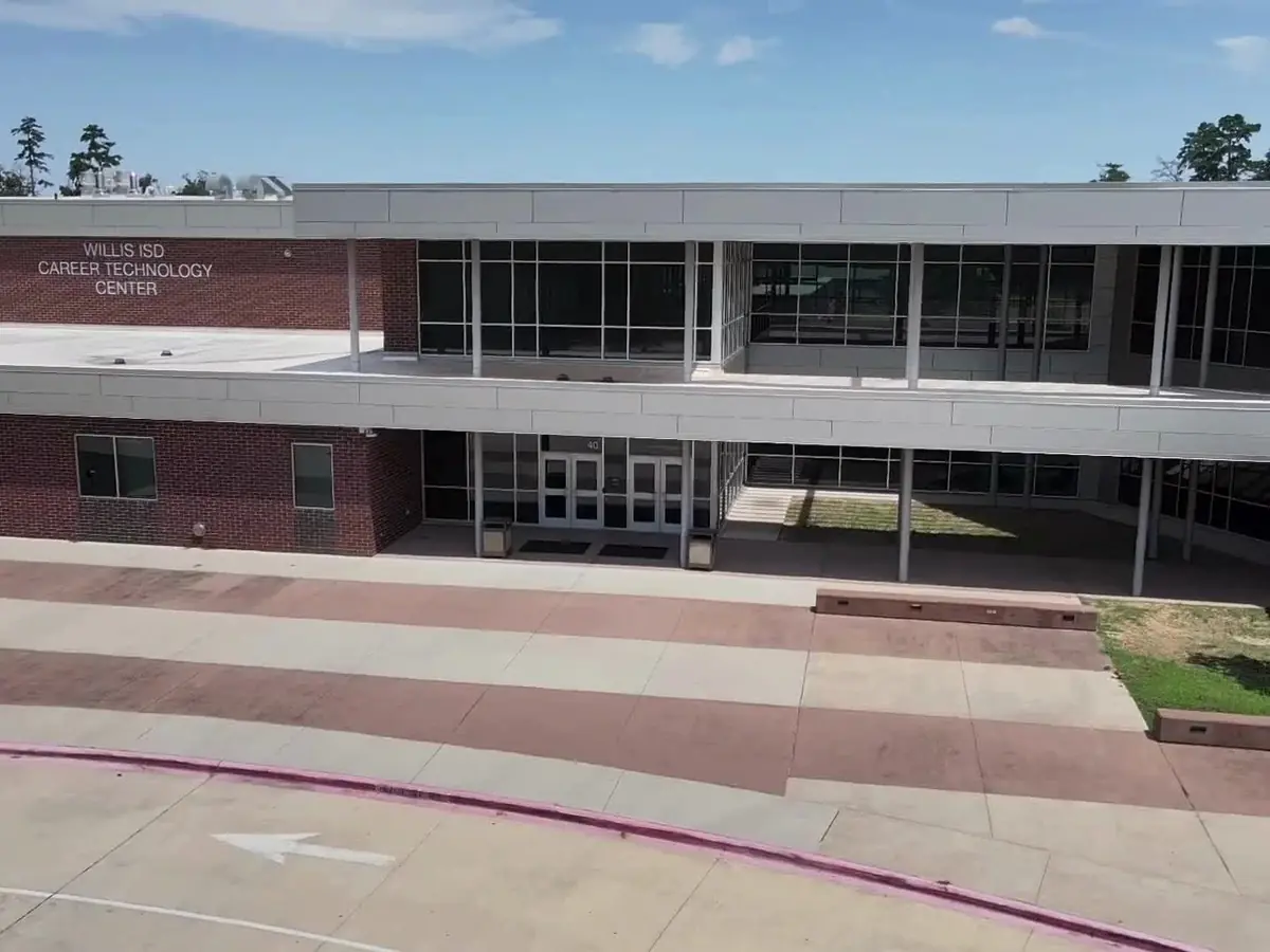 Exterior view of the two-story Willis ISD Career and Technical Education Center, with the building name displayed on the upper left facade, glass entry doors, sidewalks, and landscaped areas in front.