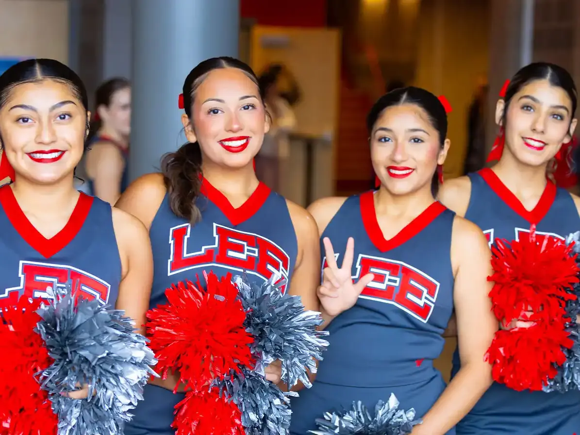 Six LEE cheerleaders in matching navy, red, and white uniforms stand indoors holding red and silver pom-poms.
