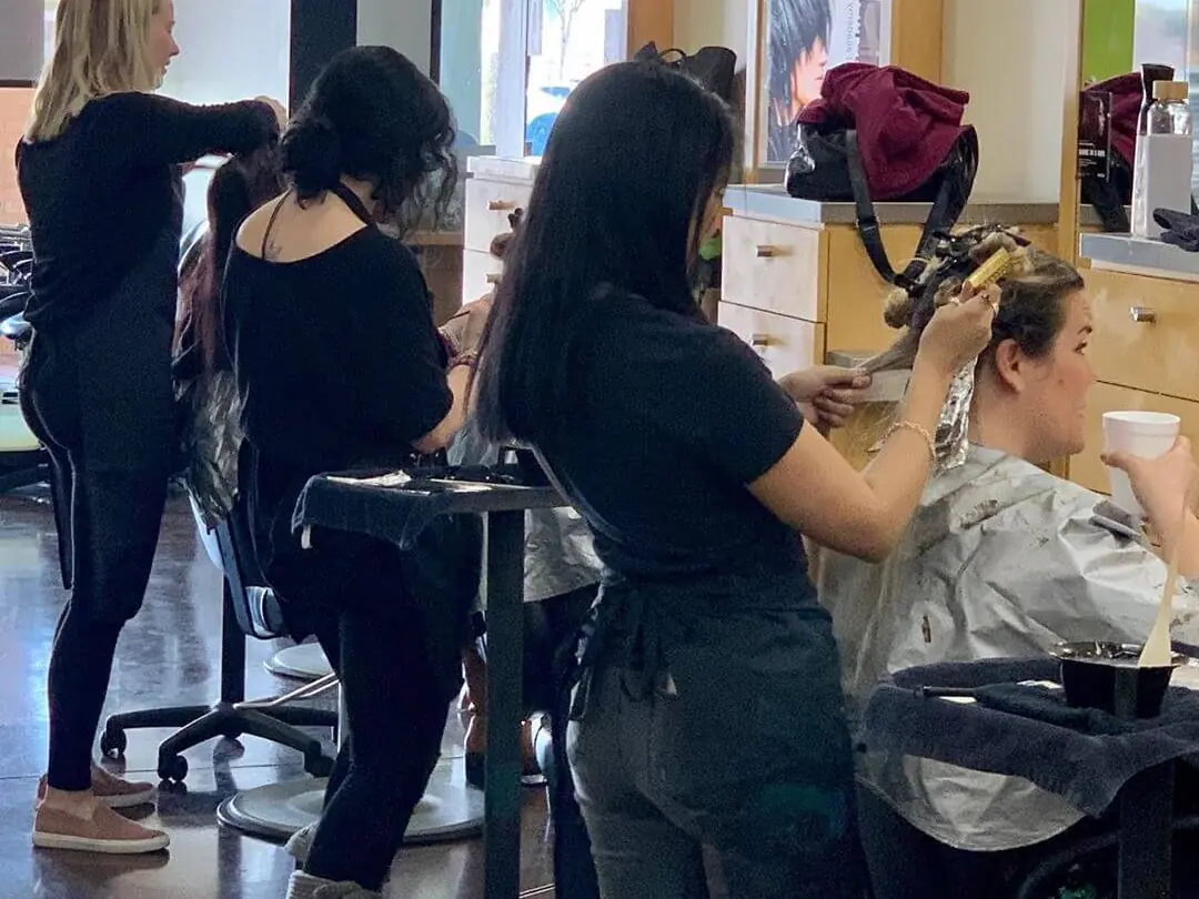 Students practice hairstyling on clients at salon stations inside the William Edge Institute cosmetology classroom.