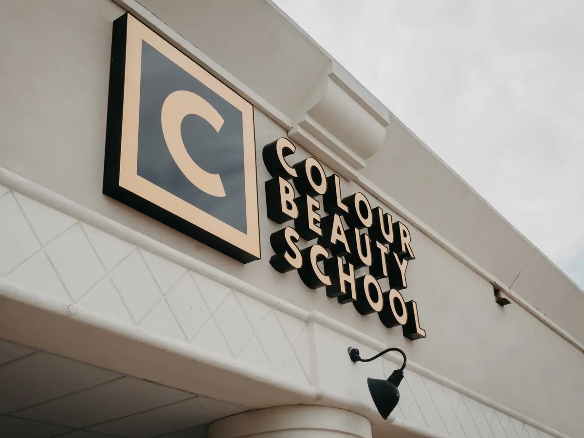 Exterior wall of Colour Beauty School with a large square C logo and raised black-and-white Colour Beauty School lettering above a doorway canopy.