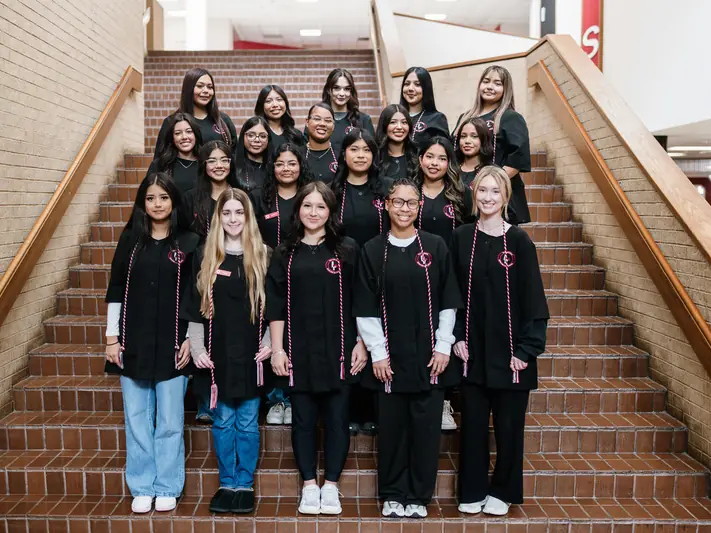 A group of cosmetology students wearing black uniforms pose together on the tiled staircase inside Greenville High School.