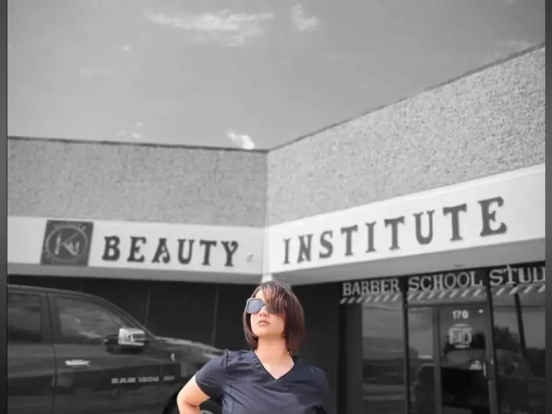 Exterior of KM Beauty Institute in a strip-mall storefront, with large BEAUTY INSTITUTE lettering above the entrance and a woman standing in front.