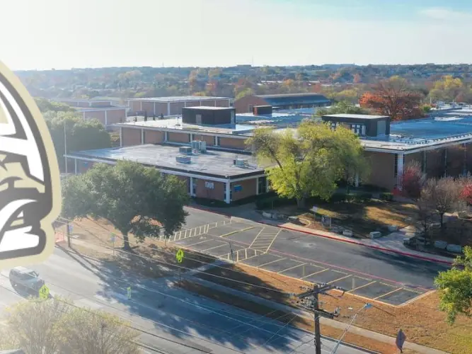 Aerial view of Navarro Early College High School campus with low school buildings, parking lots, trees, and surrounding Austin neighborhood visible from above.