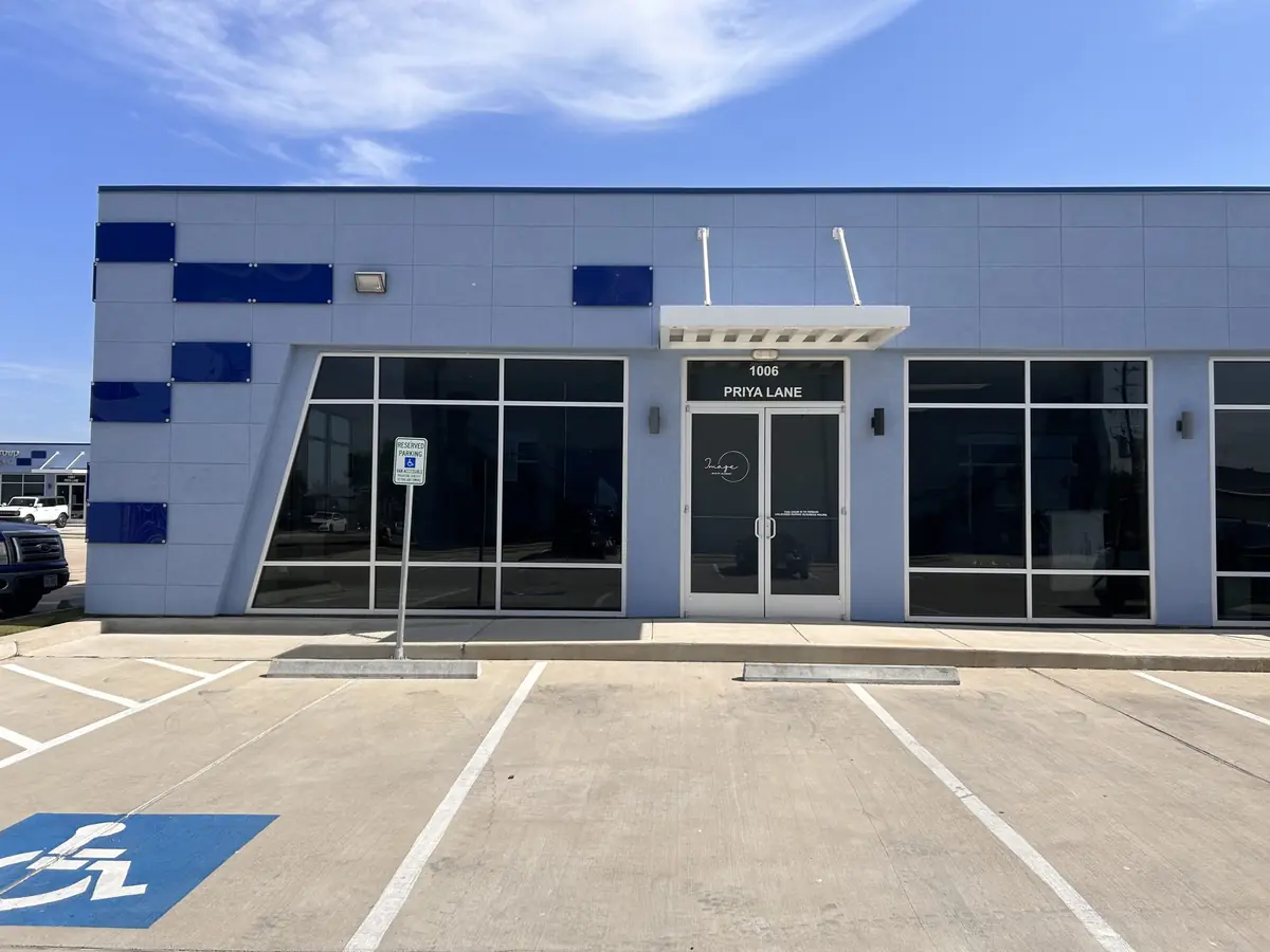 Front exterior of a modern gray Image Academy building with blue accent panels, large dark windows, a glass entrance door, and accessible parking spaces in front.