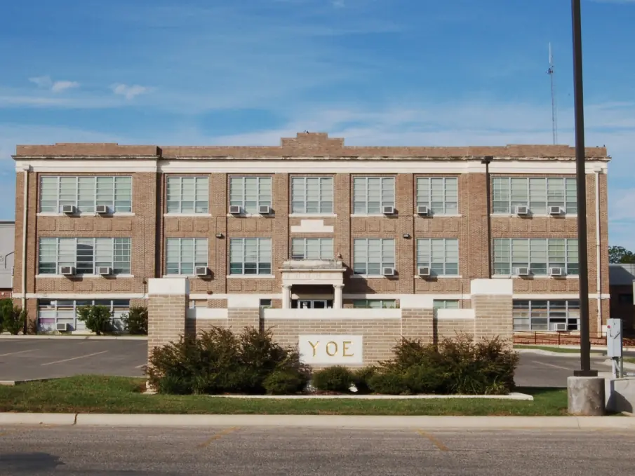 Front view of the three-story brick C.H. Yoe High School building in Cameron, Texas, with “YOE” engraved on a low wall in front.