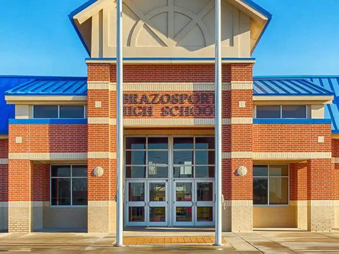Front exterior of Brazosport High School, a single-story red-brick building with bright blue roofs and a central glass entrance tower labeled Brazosport High School.