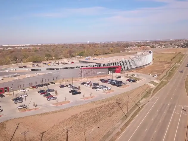 Aerial view of the Arlington ISD Career and Technical Center campus, with a large curved school building, parking lots, surrounding open land, and a multilane road alongside it.
