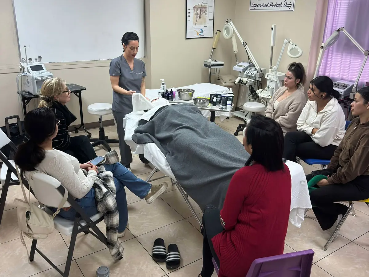 Students gather around a reclining treatment table during a practical beauty-training lesson in a classroom at 1st Academy of Beauty.