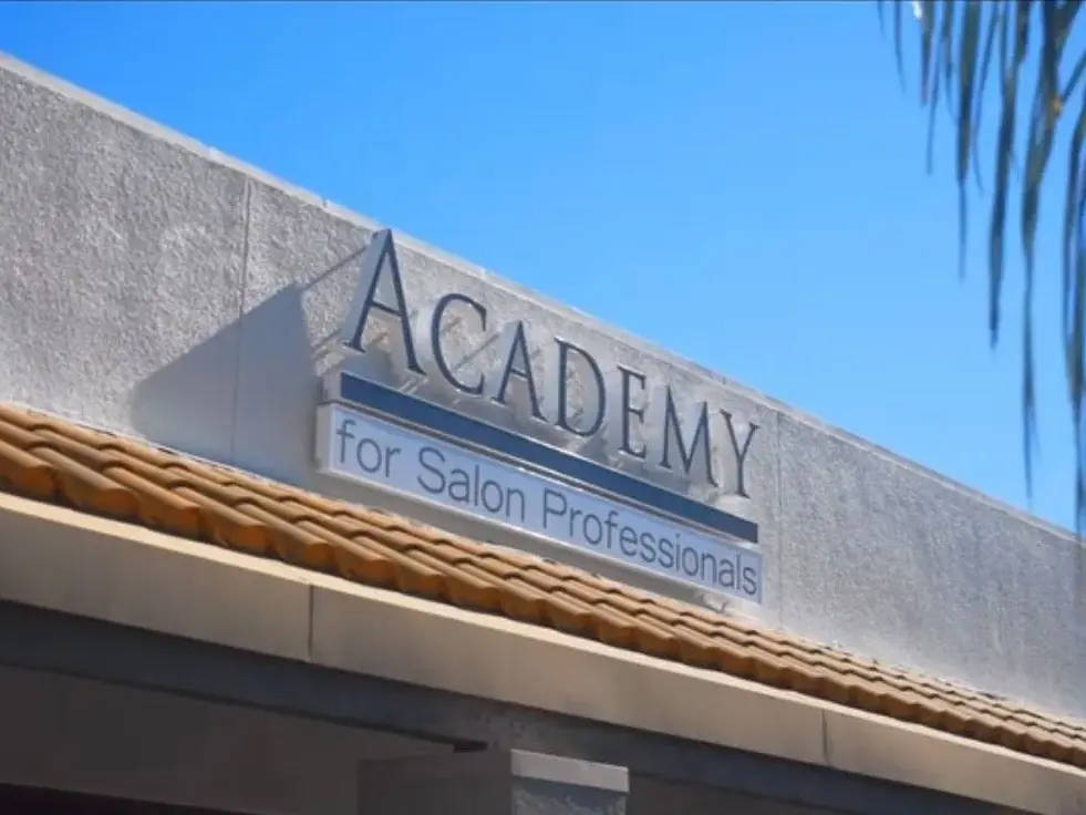 Exterior facade of Academy for Salon Professionals with the school name displayed above a tiled awning under a blue sky.