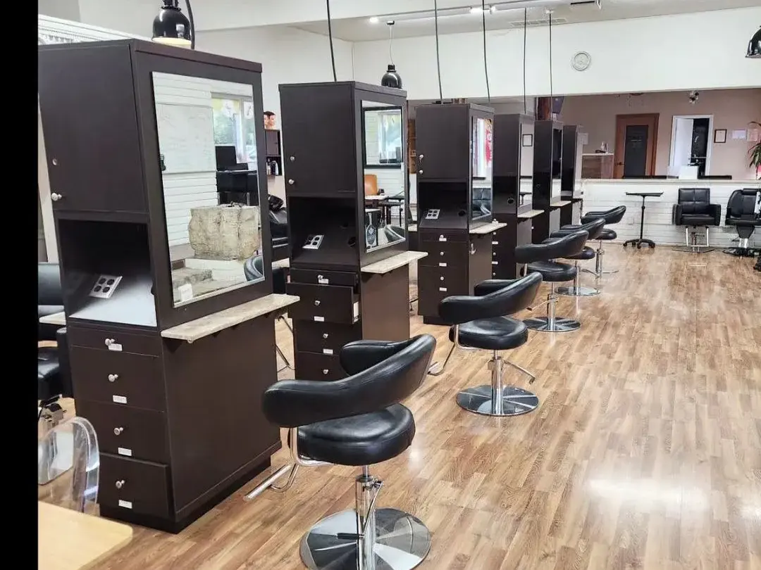 Interior of Asel Beauty College’s cosmetology salon with rows of dark styling stations, mirrors, salon chairs, and a wood-look floor.