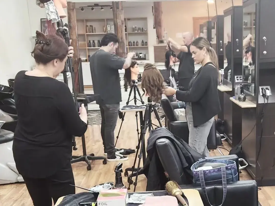 Students practice hairstyling around salon stations in the Asel Beauty College Tustin training classroom.