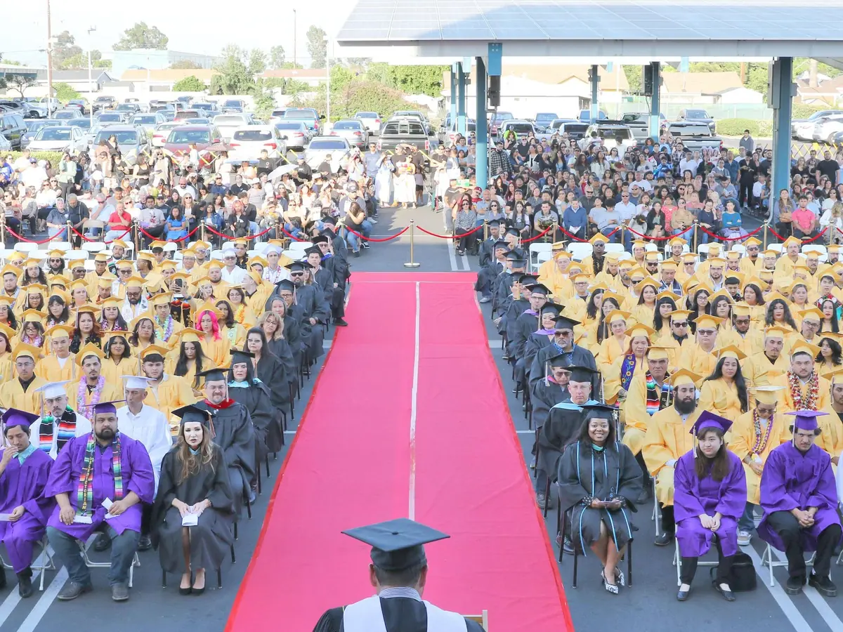 Graduation ceremony on the Baldwin Park Adult and Community Education campus, with graduates and guests seated on both sides of a red carpet leading toward a covered stage area.