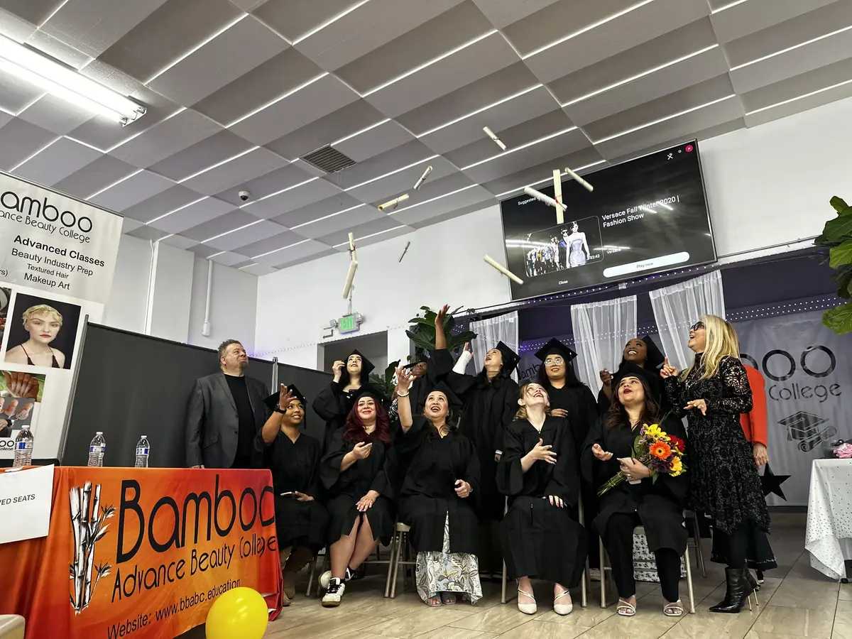 Bamboo Advance Beauty College graduation group posing indoors beside a reception desk and wall banner bearing the college name.