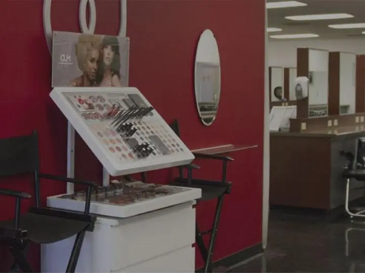 Interior of Bellus Academy’s El Cajon student salon, with styling chairs and mirrors along the right wall and a red display wall with oval mirrors and a central product stand.