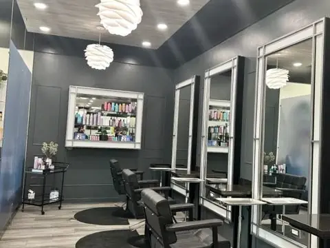 A modern hair-styling studio with black salon chairs, mirrors, styling stations, product shelves, and pendant lights.