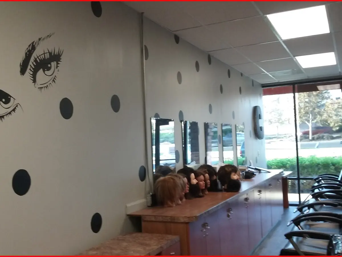 Interior of CEN Beauty Academy's salon with styling chairs, mirrors, mannequin heads on a counter, and large eye artwork on the wall.