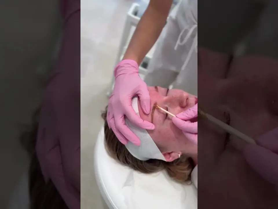 A practitioner wearing pink gloves performs an esthetic treatment on a client reclining in a treatment chair.