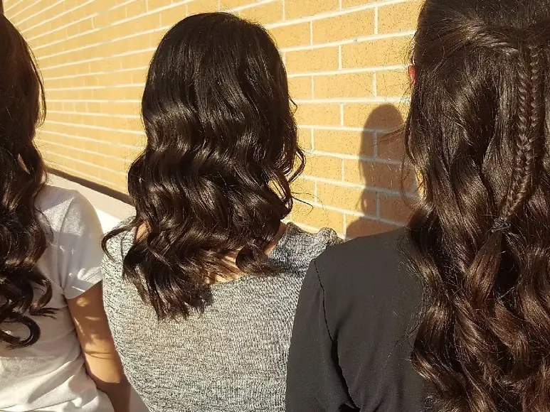 Three students shown from behind with long styled hair standing in front of a brick wall.