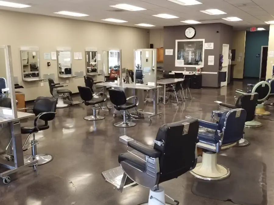 Interior of Hinton Barber and Beauty College's barbering classroom with rows of styling stations, mirrors, barber chairs, and equipment.