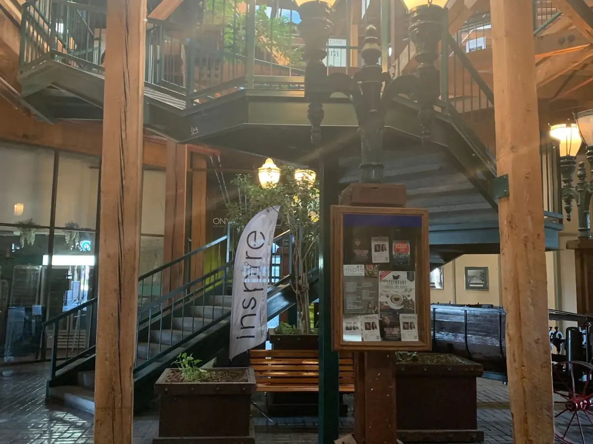 Interior entrance area with wooden beams, brick flooring, hanging lanterns, a staircase, and an Inspire banner.