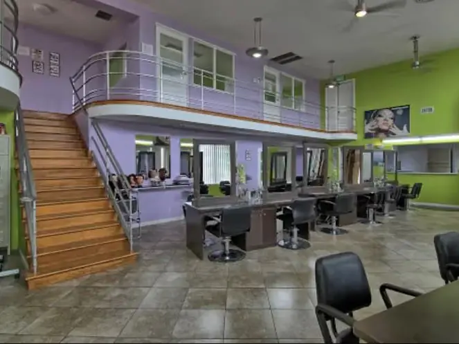 Interior of a beauty school salon with styling stations, mirrors, a wooden staircase, and a mezzanine level.