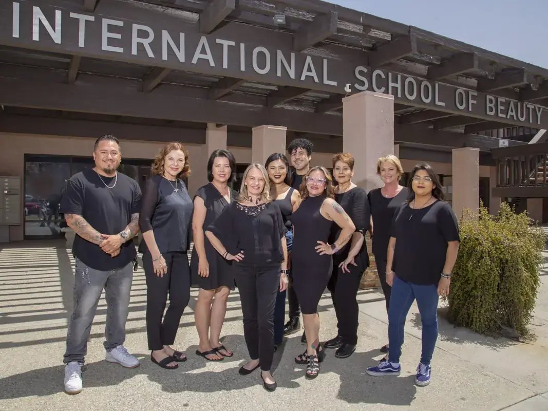 A group of staff members standing outside beneath a large sign reading “INTERNATIONAL SCHOOL OF BEAUTY.”