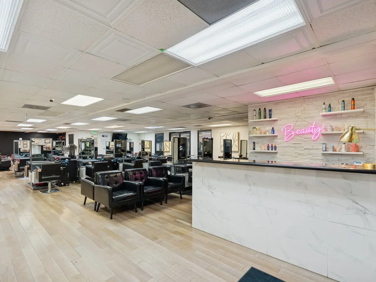 Interior of Monarch Beauty Academy showing rows of salon styling stations, black chairs, mirrors, product shelves, and a white reception counter with a pink Beauty sign.