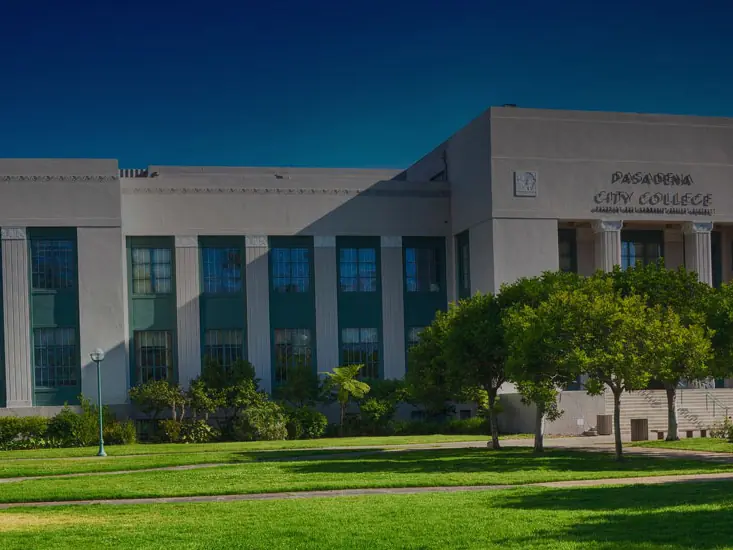 Exterior of a Pasadena City College building with a broad white facade, tall blue windows, trees, and a lawn in front.