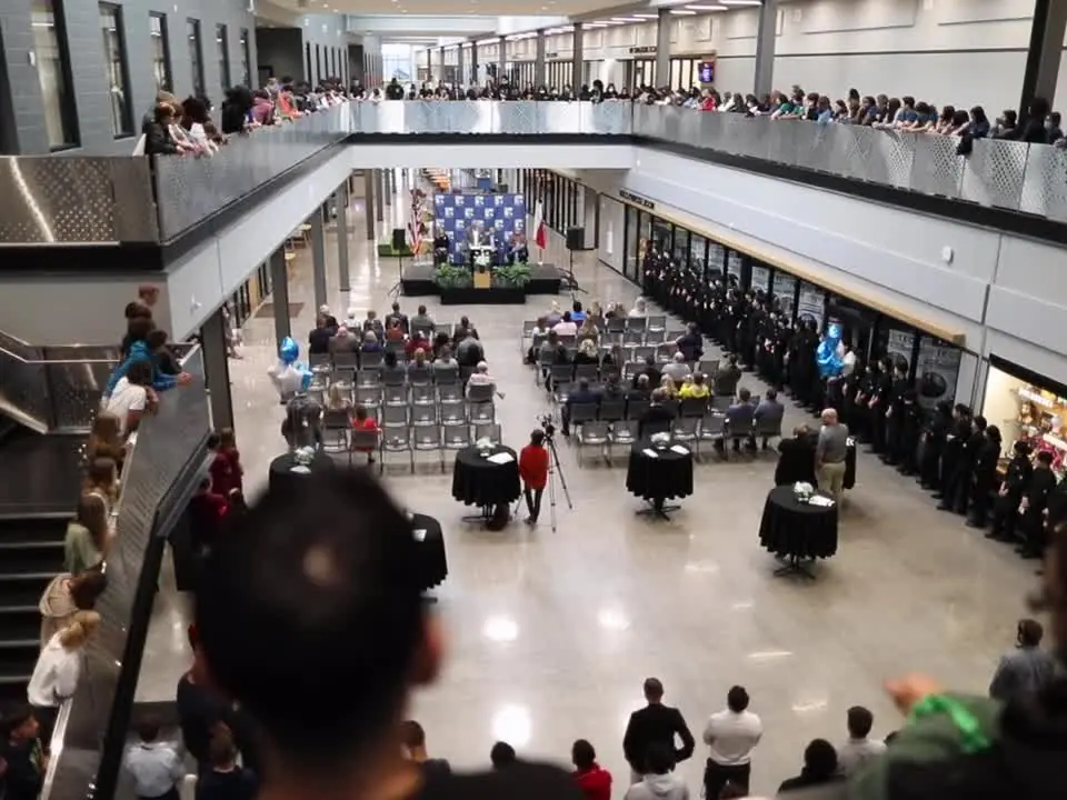 Wide view of a bright, multi-level Technology, Exploration and Career Center atrium with balconies crowded with spectators, tables arranged on the lower floor, and an event taking place in the center.