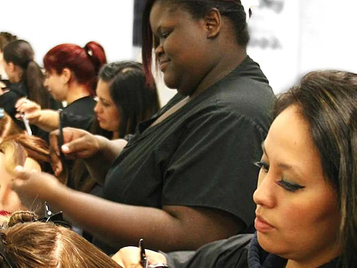 Students practice hairstyling on mannequin heads in a cosmetology classroom.